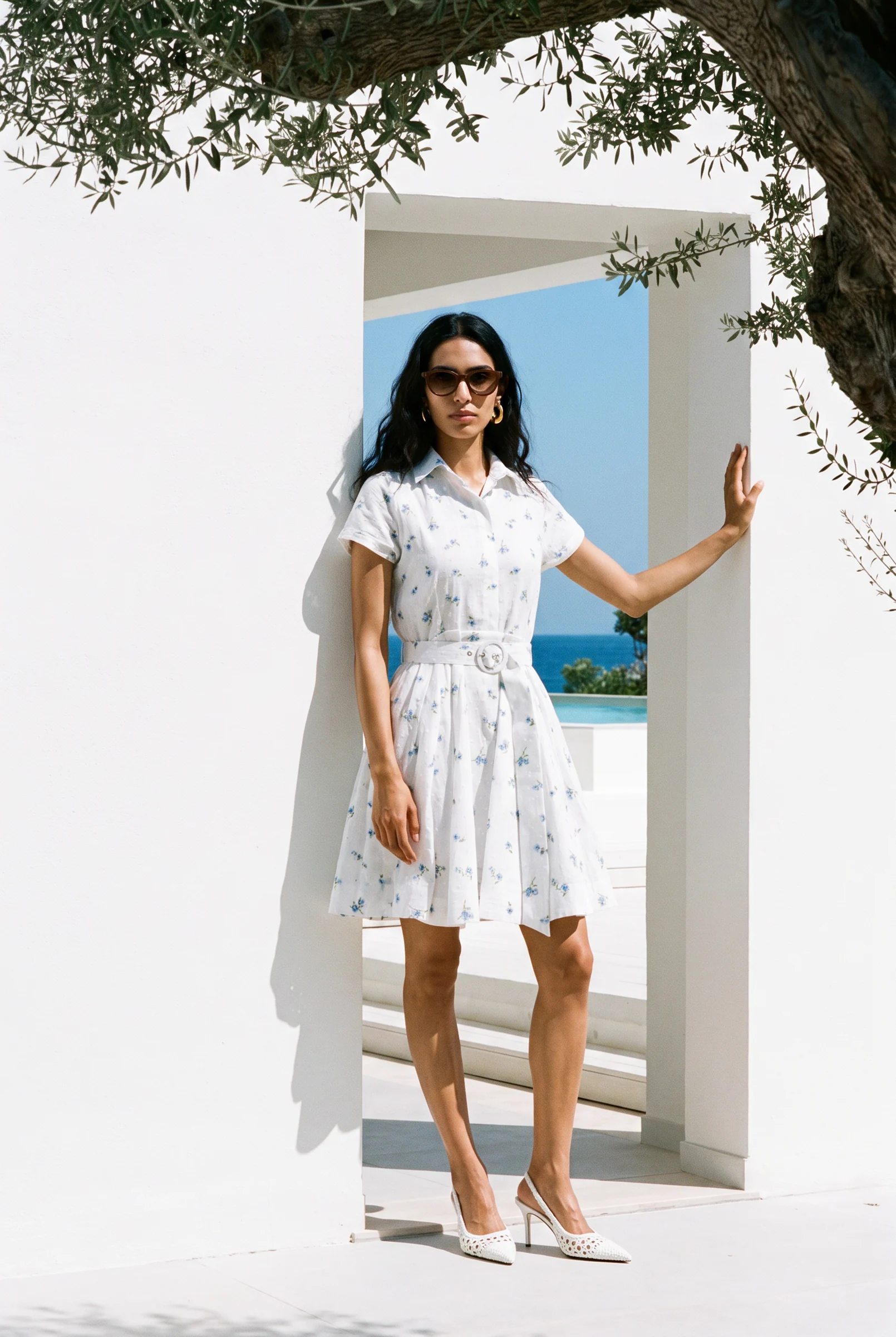 Full length: the shirt dress in a white doorway, the sea behind and an olive branch overhead