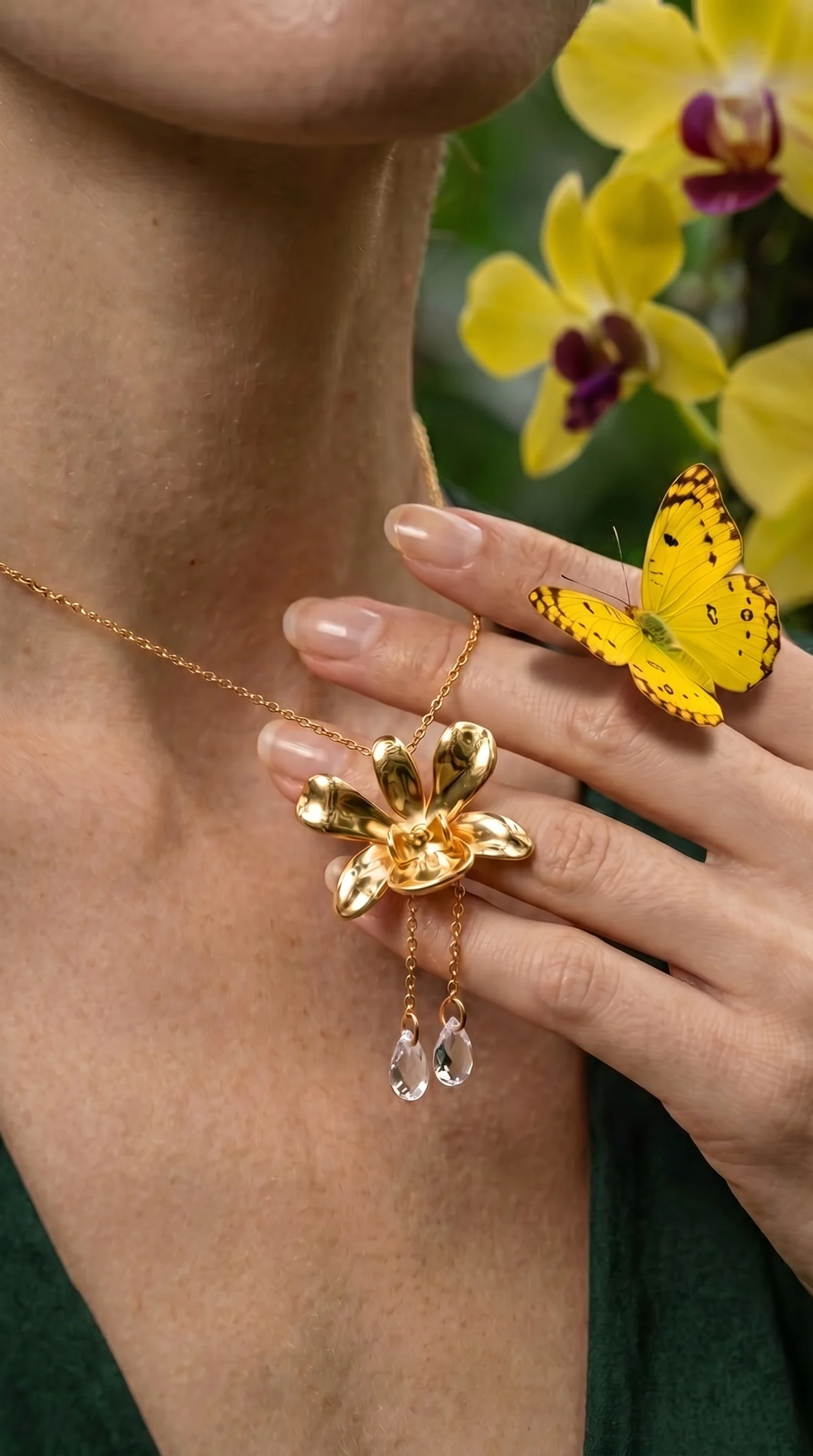 A hand at the collarbone touching a gold orchid pendant, a yellow butterfly on the fingers