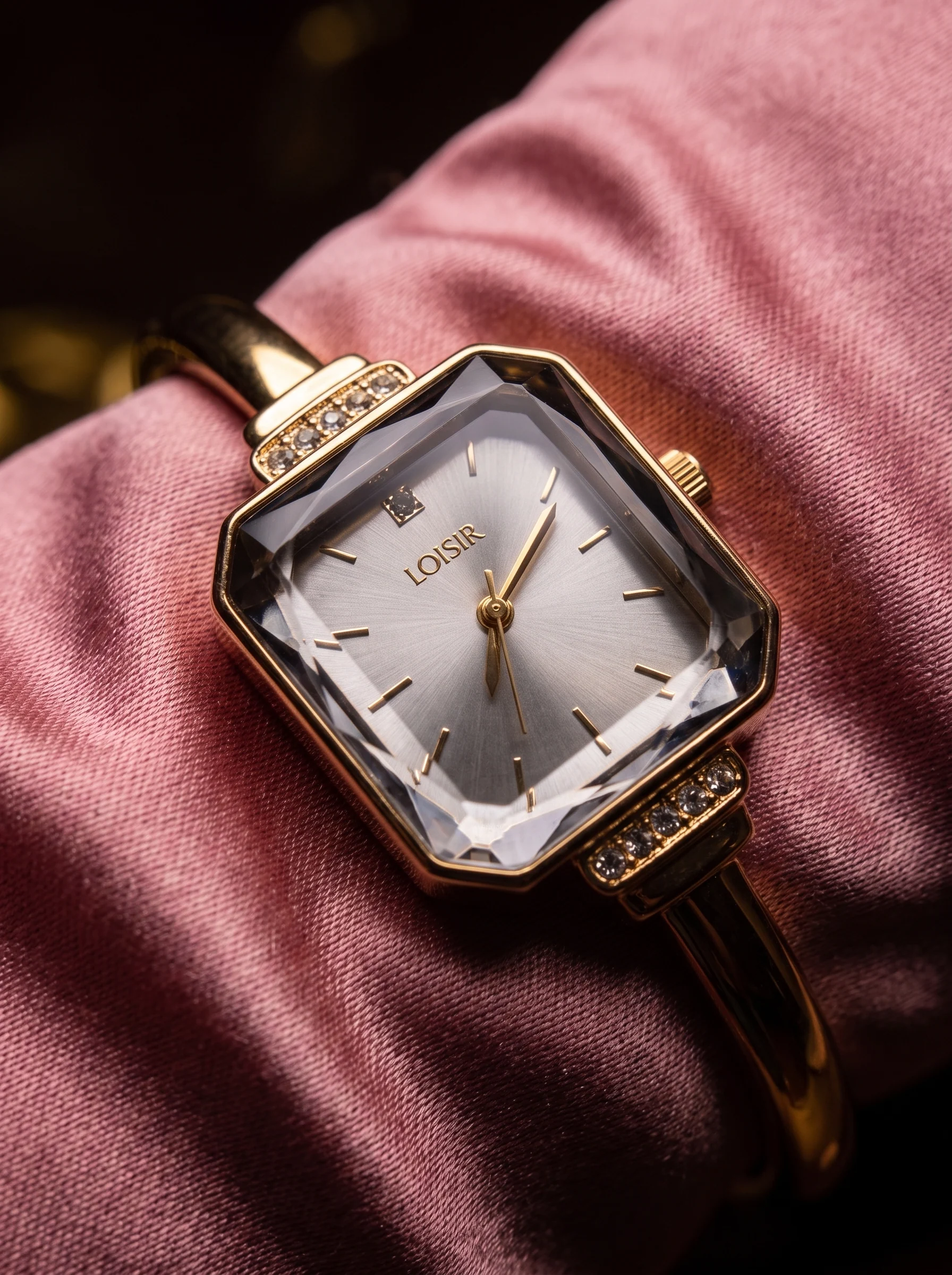 A gold bracelet watch with a faceted rectangular crystal on a pink satin glove